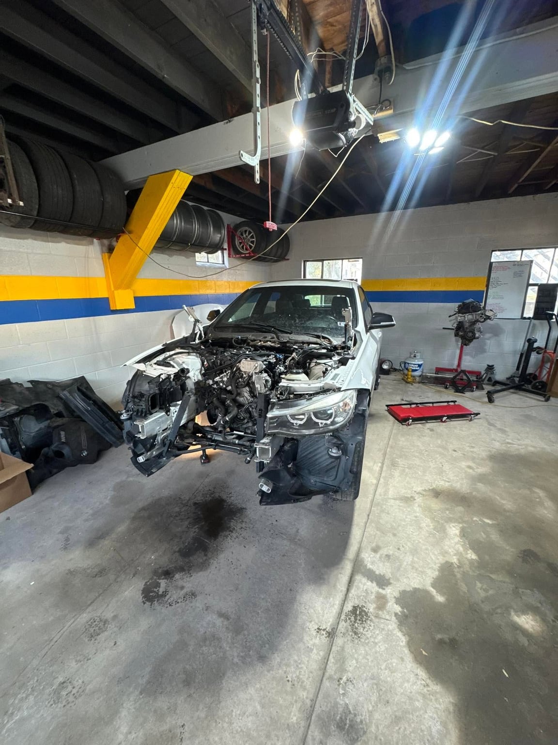 Car in a workshop bay with its front end removed and an engine on a nearby stand