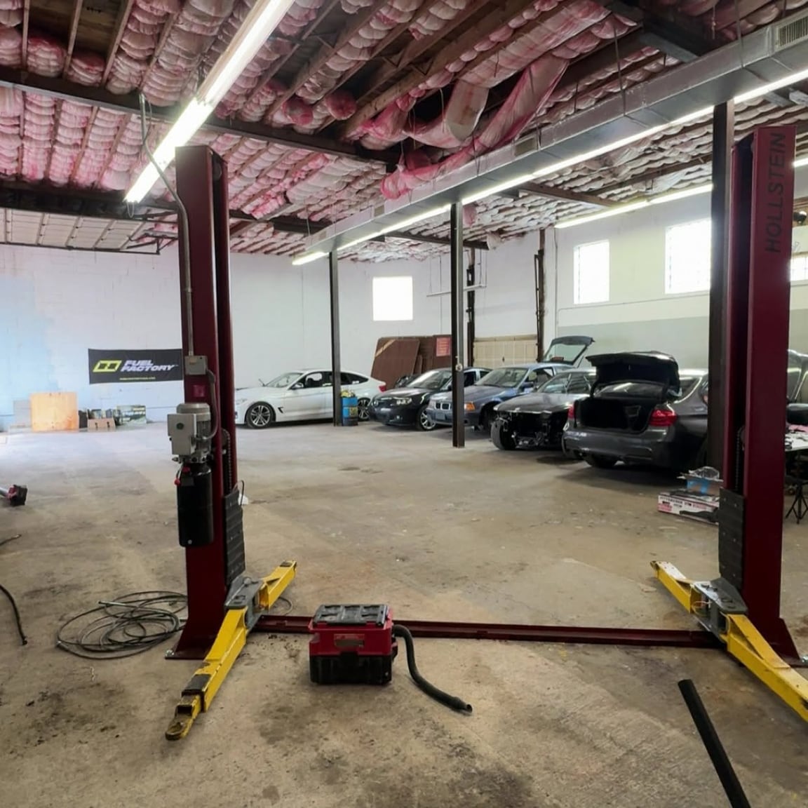 View through a red two-post lift toward cars parked across the workshop