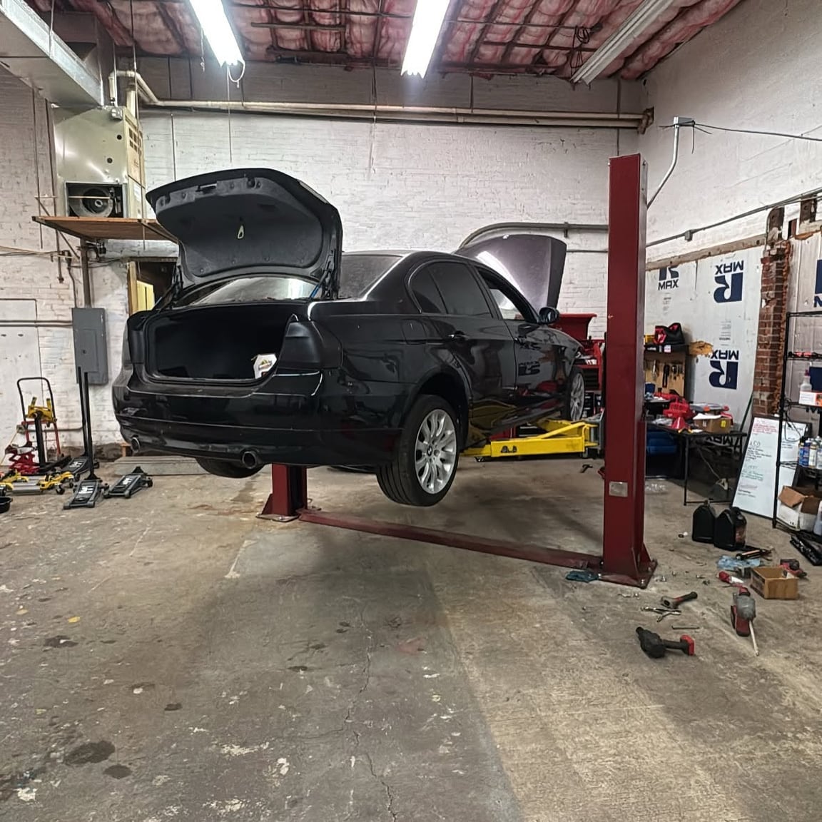 Dark car raised on a red two-post lift with its hood and rear hatch open