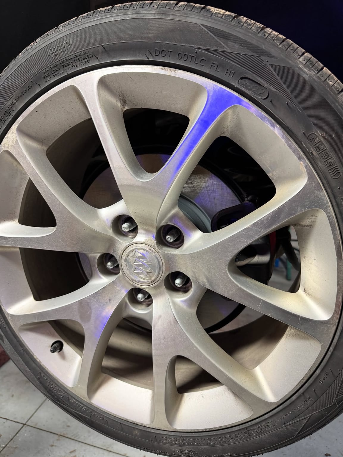 Silver multi-spoke wheel and tire lit by a blue reflection